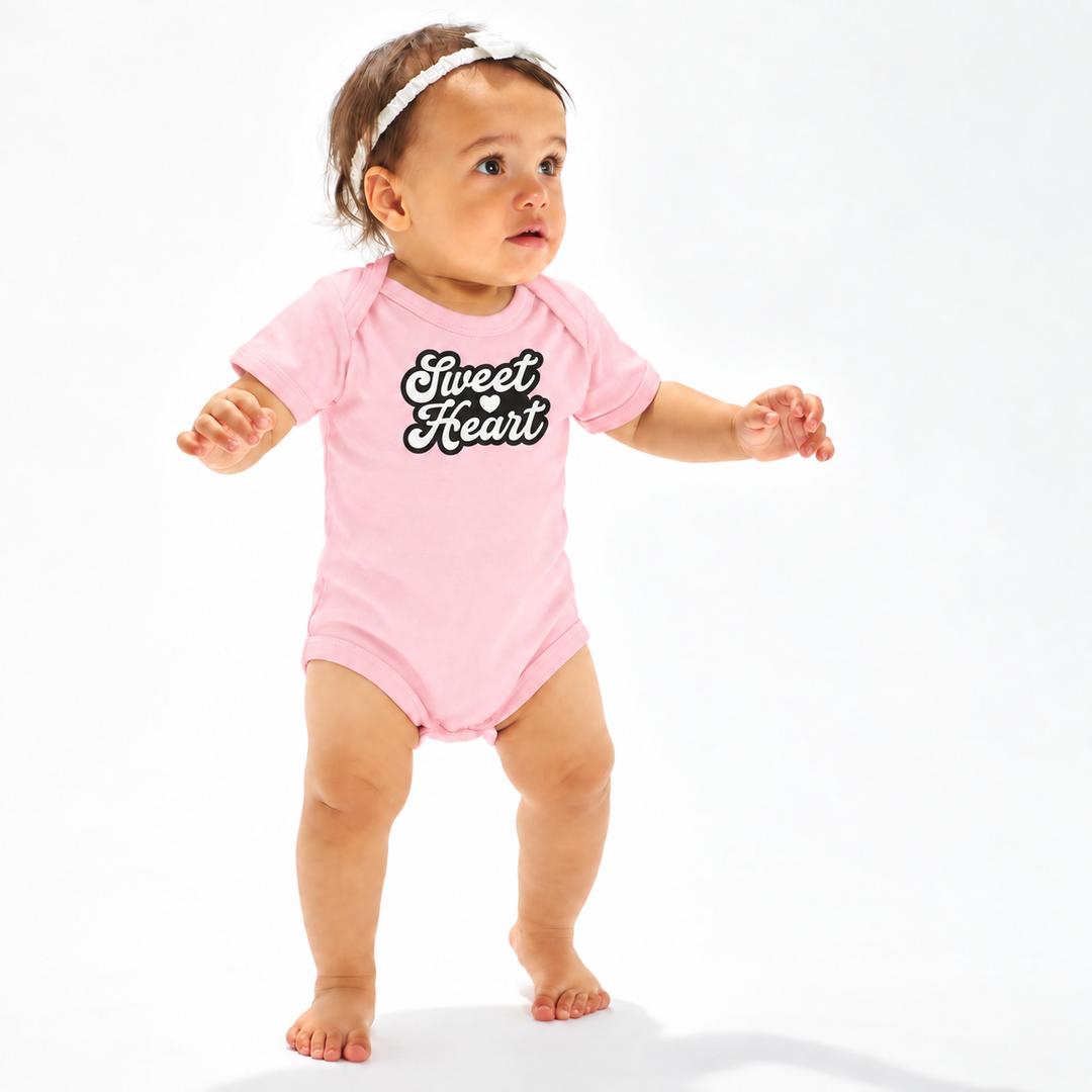 Baby draagt roze baby romper met Sweet Heart tekst en hartje.