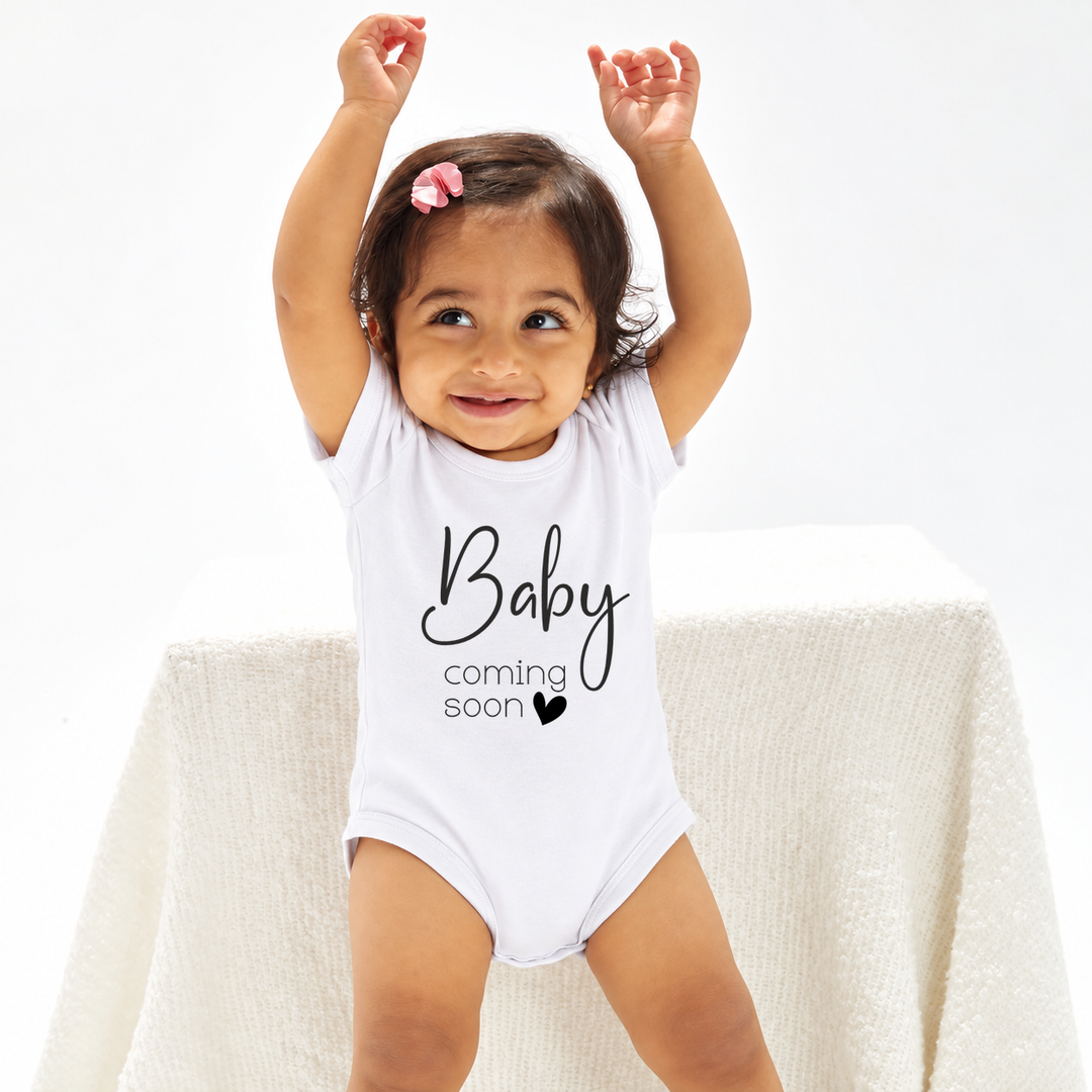 Baby draagt witte romper met tekst Baby Coming Soon.