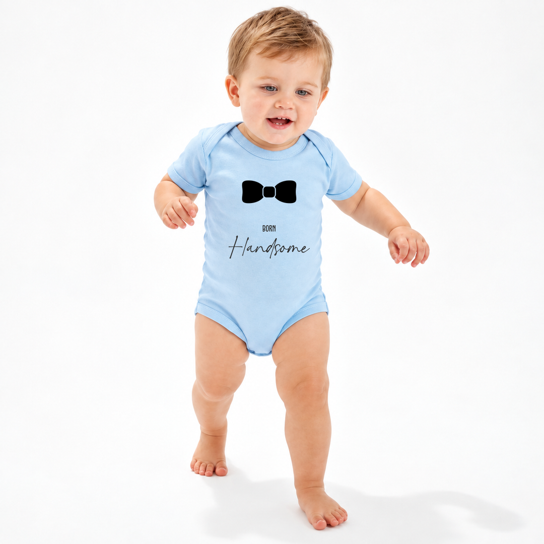 Baby draagt blauwe baby romper met Born Handsome opdruk.