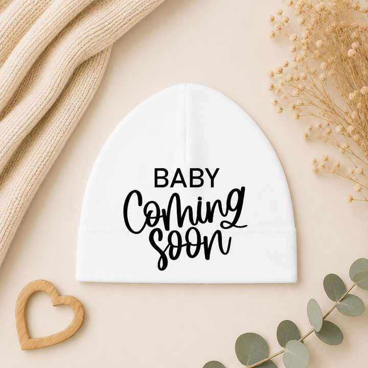 Wit babymutsje met tekst “Baby Coming Soon” – zwangerschap aankondigen met mutsje