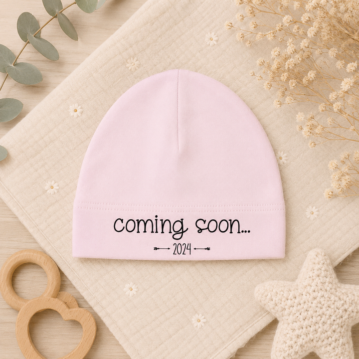 Roze babymutsje met tekst “coming soon…” van organic katoen, leuk voor zwangerschapsaankondiging of kraamcadeau