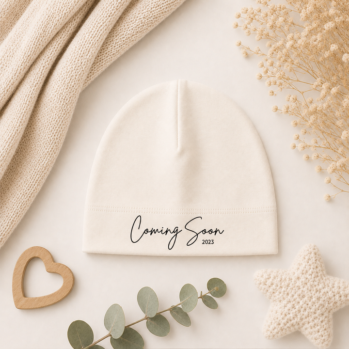 Close-up van wit mutsje met tekst “Coming Soon…”, zacht babymutsje van organic katoen