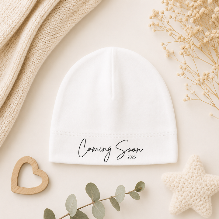 Wit babymutsje met tekst “Coming Soon…” van organic katoen, leuk voor zwangerschap aankondigen of als kraamcadeau