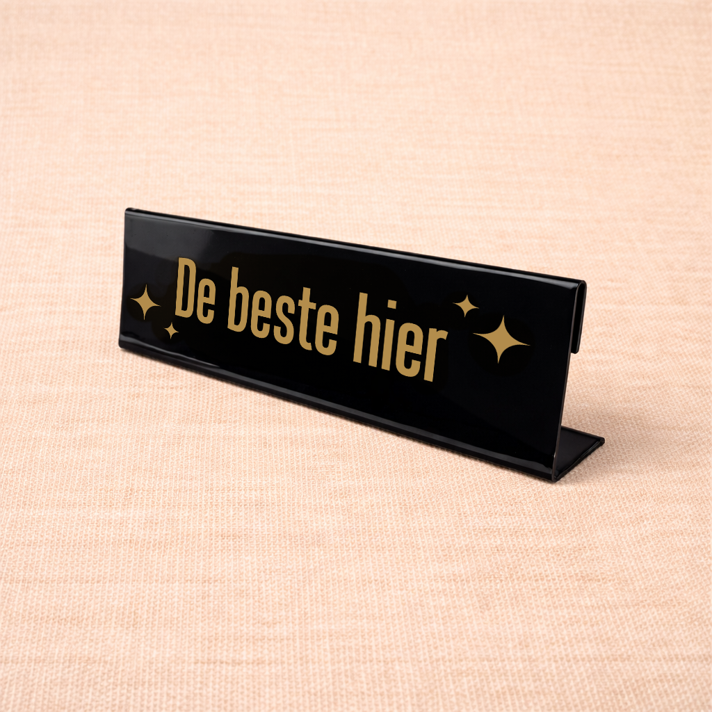 Zwart bureau naambordje met tekst “De beste hier” als grappig kantooraccessoire