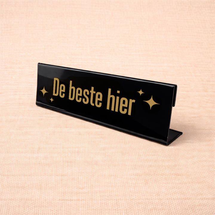 Zwart bureau naambordje met tekst “De beste hier” als grappig kantooraccessoire