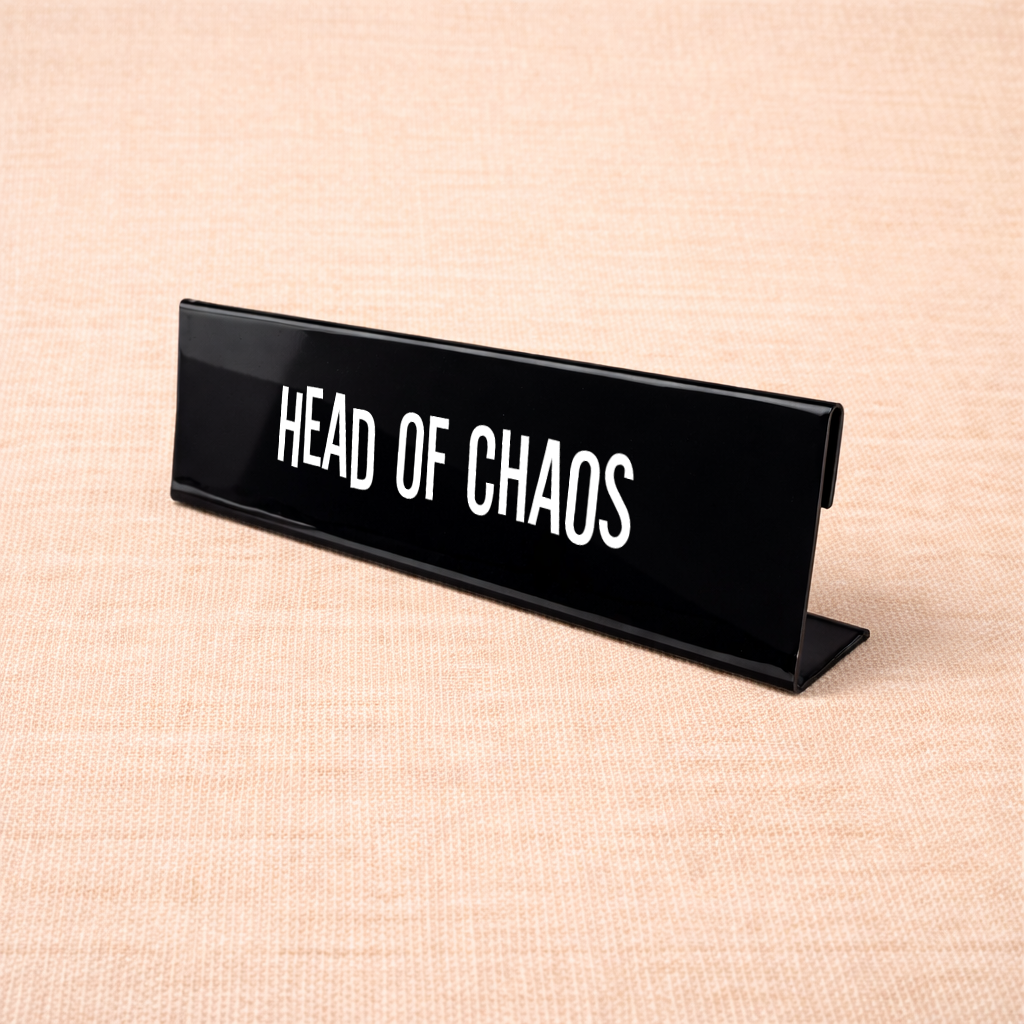 Zwart bureau naamplaatje met tekst “Head of chaos” op een bureau