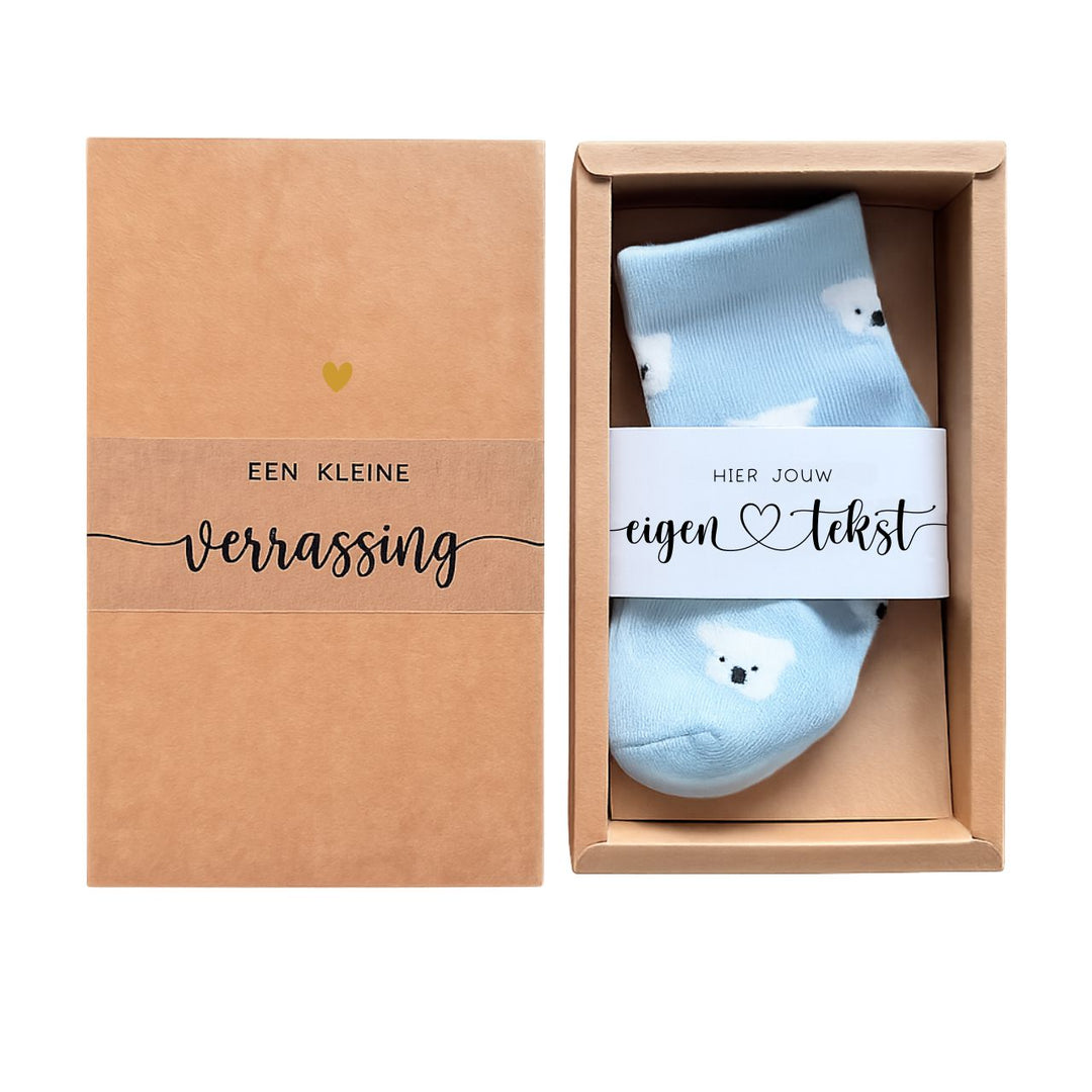 Luxe cadeauverpakking met blauwe baby sokjes voorzien van een gepersonaliseerde wikkel met eigen tekst – perfect als klein kraamcadeautje of verrassing