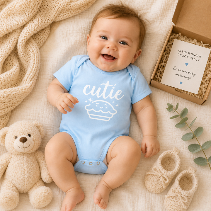 Lachende baby draagt babyblauw “cutie” rompertje met cupcake print, ideaal als kraamcadeau en babyfoto outfit
