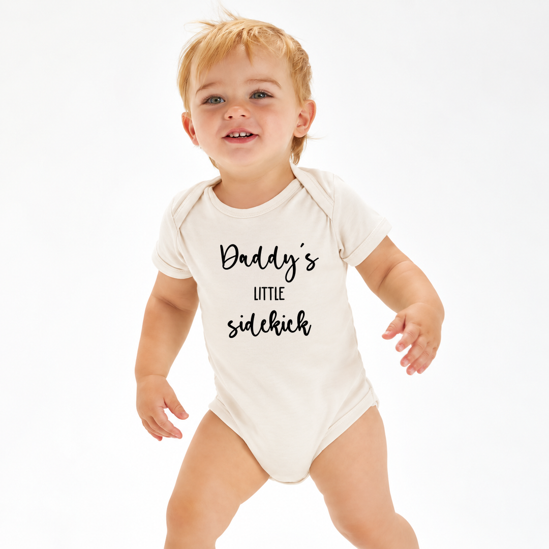 Baby in naturel romper met tekst Daddy’s Little Sidekick.