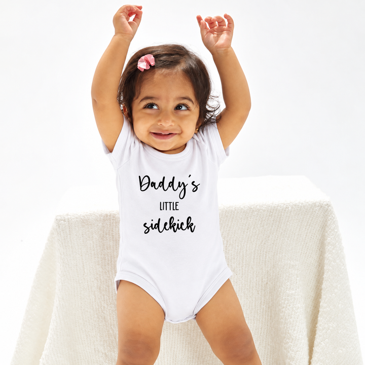 Baby in witte romper met tekst Daddy’s Little Sidekick.