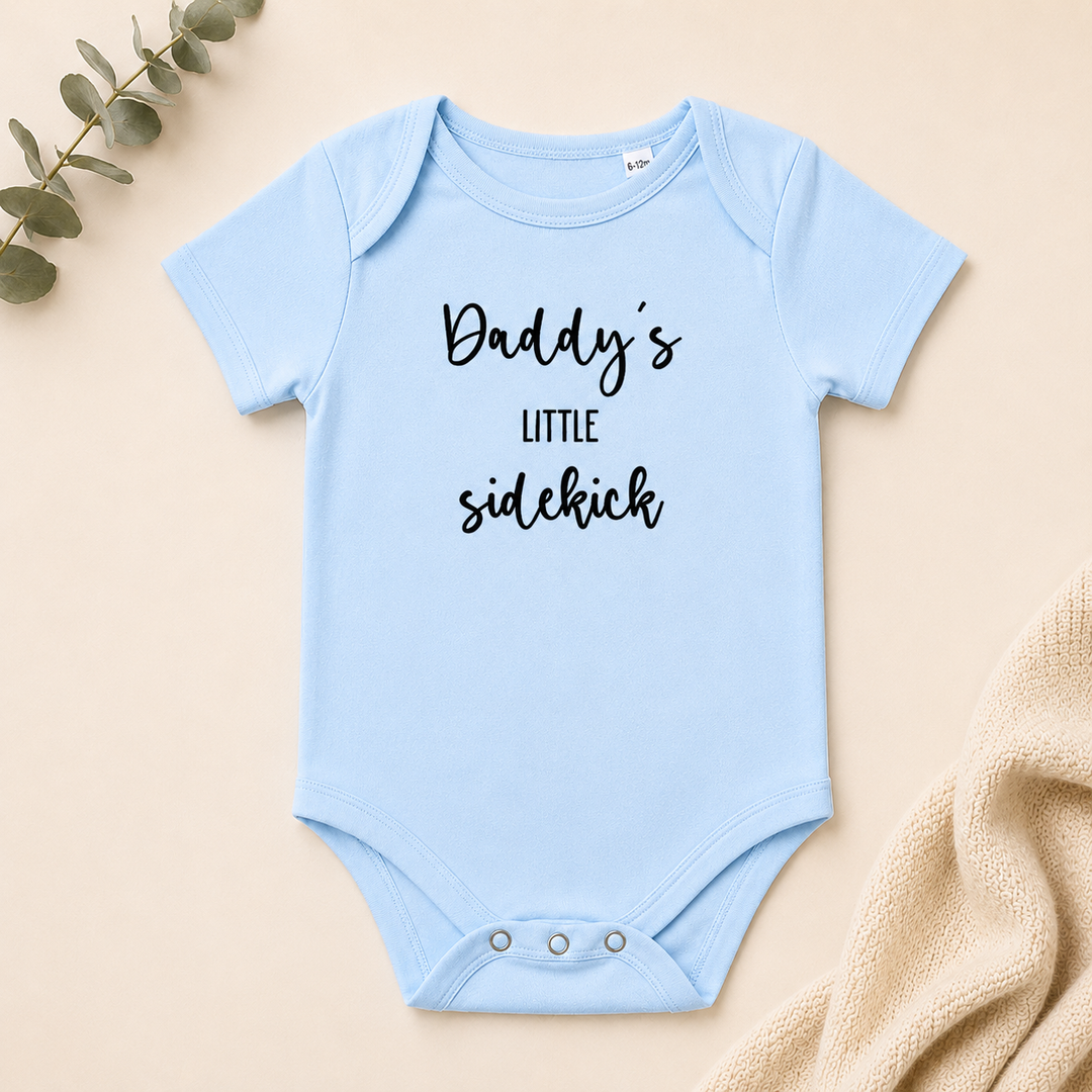 Babyblauw rompertje met tekst “Daddy’s little sidekick” – grappige zwangerschapsaankondiging en kraamcadeau van biologisch katoen