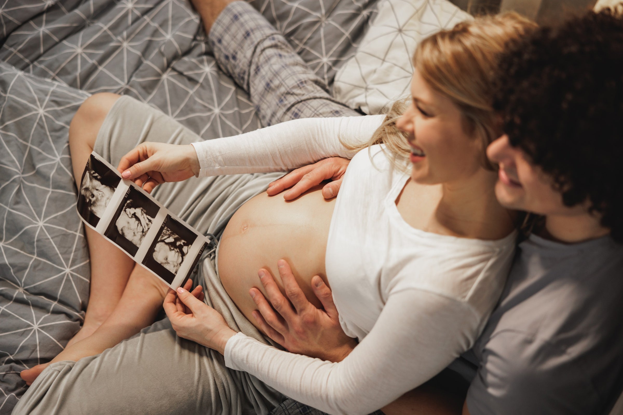 “Aanstaande ouders op bed bekijken een echo van hun baby terwijl ze de zwangere buik vasthouden – een intiem moment van verwachting en verbondenheid”