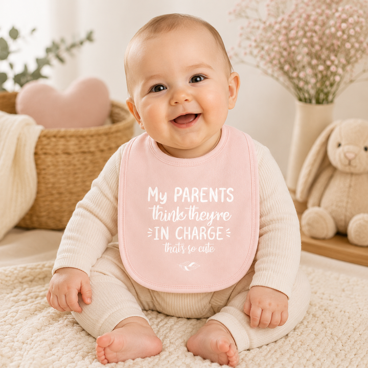 Baby draagt slabbetje met tekst “My parents think they’re in charge, that’s so cute” – origineel babycadeau en grappige slab met tekst