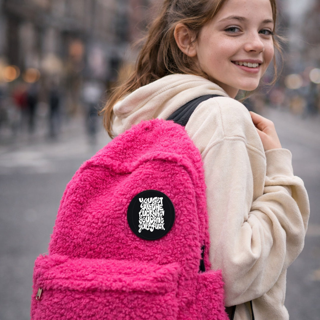 Zwarte quote button op roze rugzak – tekst: “You get all the luck…”