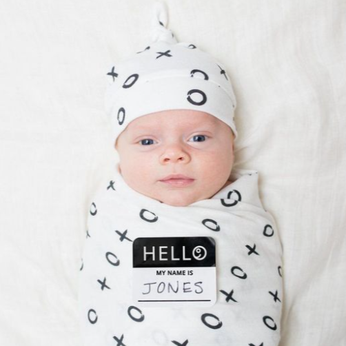 Newborn baby ingepakt in Lulujo Hello World swaddle Hugs & Kisses met bijpassend mutsje en Hello geboortesticker, ideaal als kraamcadeau