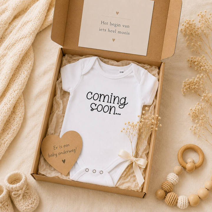Wit baby rompertje met tekst “coming soon…” in cadeaubox met kaartje en babyaccessoires – originele zwangerschapsaankondiging cadeau voor opa en oma