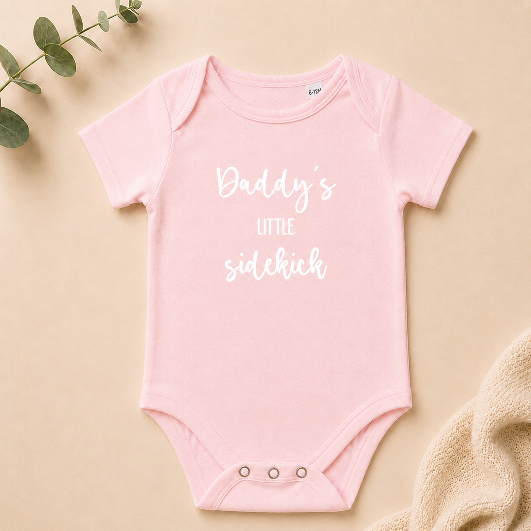 Lichtroze rompertje “Daddy’s little sidekick” als grappig rompertje met tekst voor babyshower of zwangerschap aankondigen
