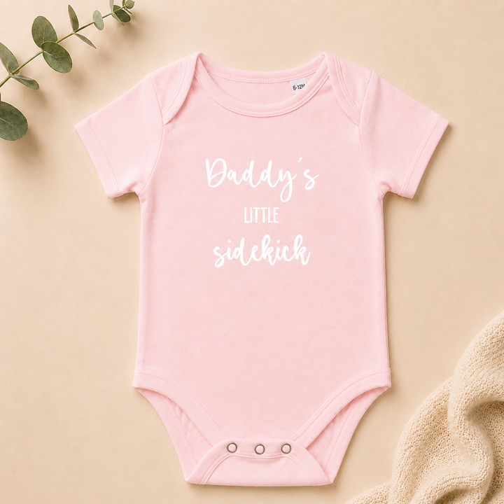 Lichtroze rompertje “Daddy’s little sidekick” als grappig rompertje met tekst voor babyshower of zwangerschap aankondigen