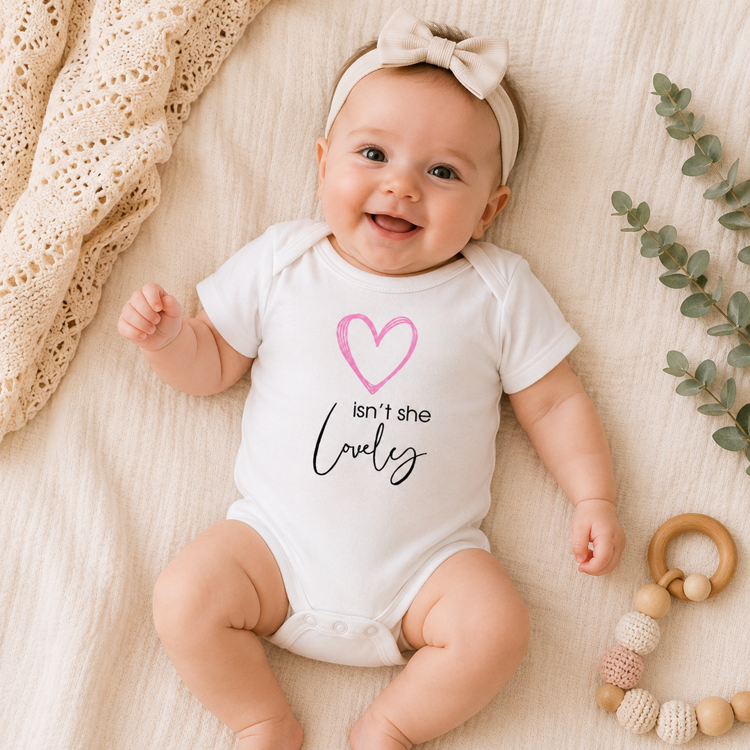 Baby draagt wit rompertje met tekst “isn’t she lovely” en roze hartje – lief babycadeau / kraamcadeau rompertje met tekst