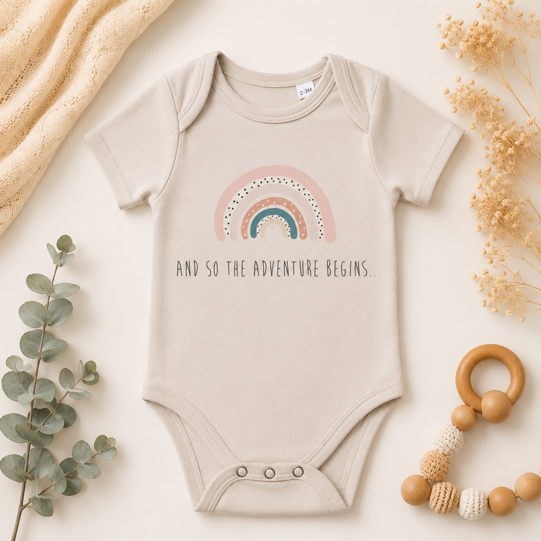 Beige babyrompertje met regenboog print en tekst “jij is de mooiste regenboog”, ideaal als zwangerschapsaankondiging of kraamcadeau