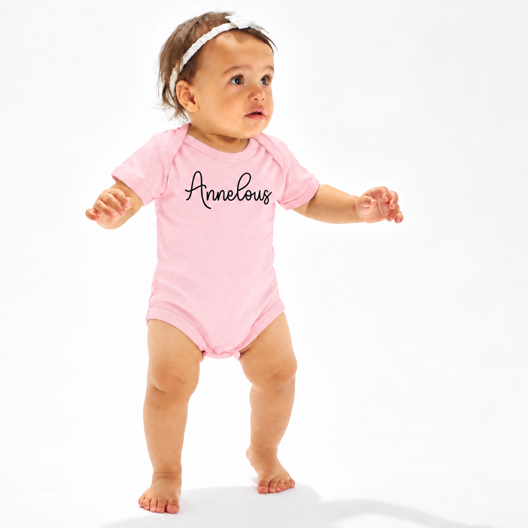 Baby draagt roze romper met naam Annelous op de voorkant.