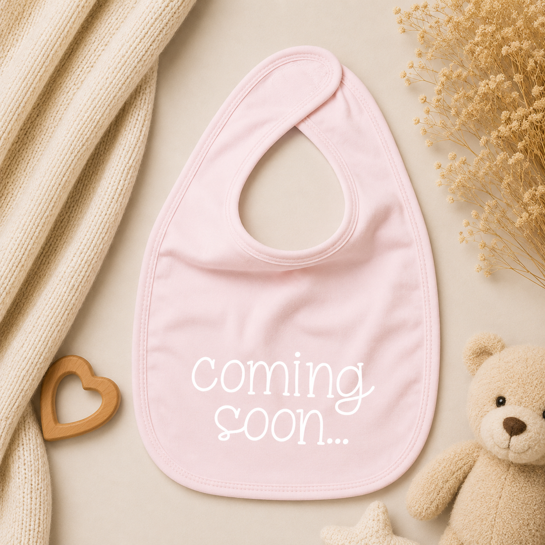Roze baby slabbetje met tekst “coming soon…” voor zwangerschap aankondigen aan familie