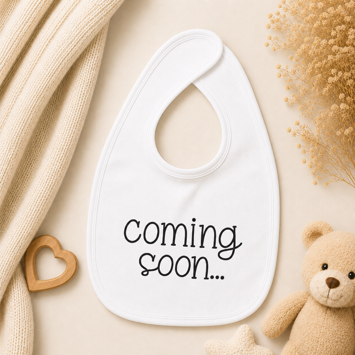 Wit baby slabbetje met tekst “coming soon…” voor een originele zwangerschapsaankondiging