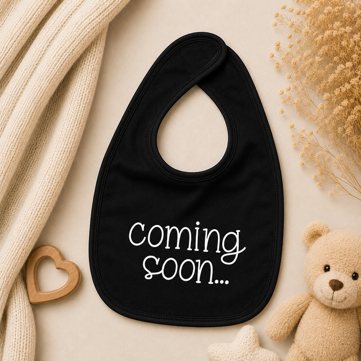 Zwart baby slabbetje met tekst “coming soon…” als originele zwangerschapsaankondiging