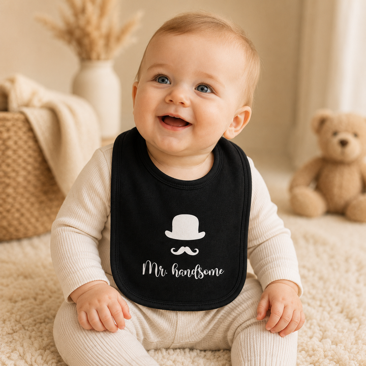 Baby draagt zwart slabbetje met tekst “Mr. handsome”, zacht bandana slabbetje van organic katoen