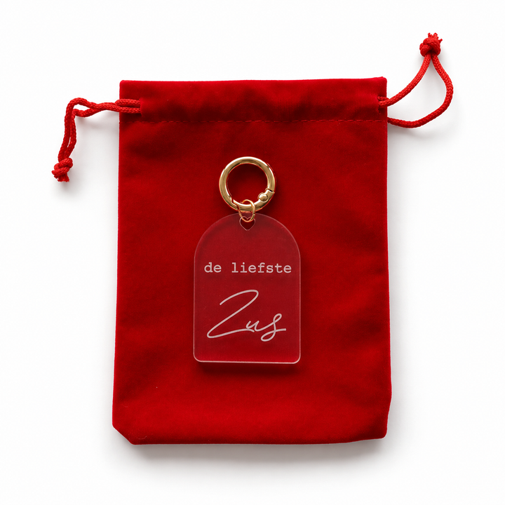 Transparante sleutelhanger met tekst de liefste zus frontaal op rood cadeauzakje.