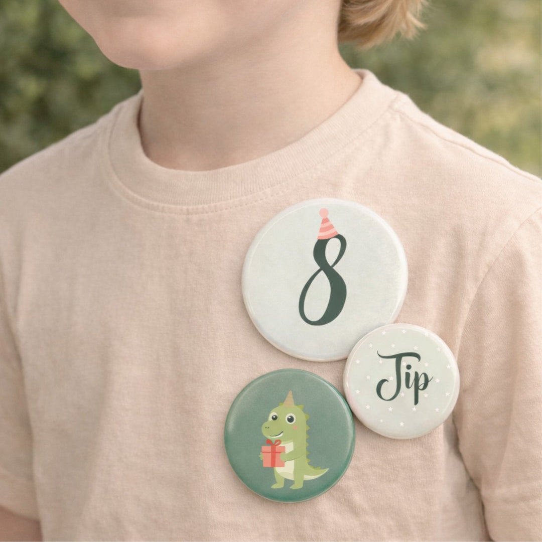 Drie gepersonaliseerde verjaardagsbuttons met het getal 8, de naam Jip en een dinosaurusillustratie, gedragen op een beige shirt door een kind.