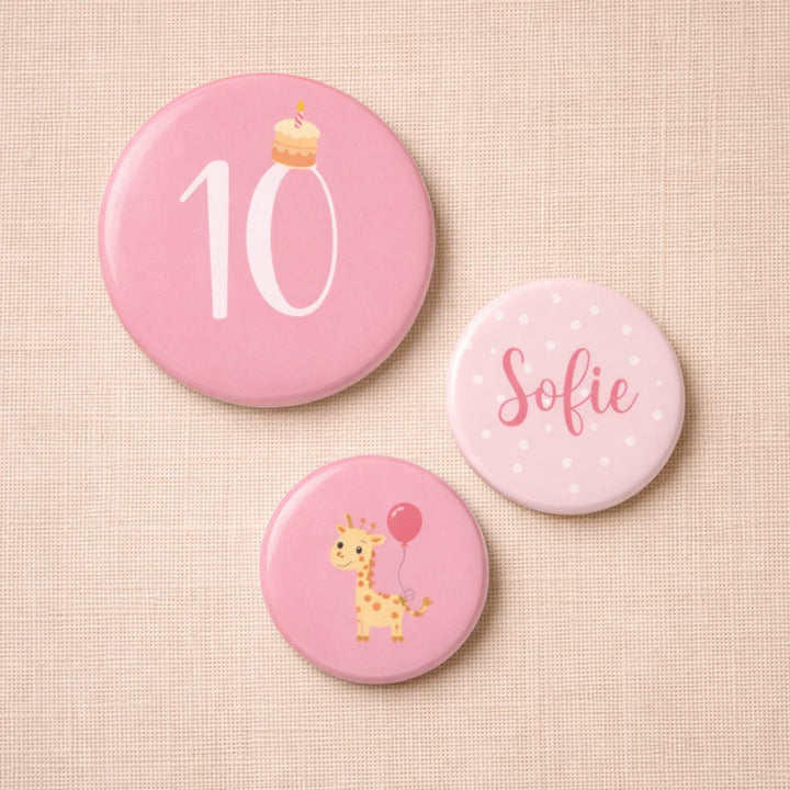 Set van drie gepersonaliseerde verjaardagsbuttons voor een meisje van 10 jaar met het getal 10, de naam Sofie en een giraf met ballonnen, in zachte roze tinten op een stoffen achtergrond.