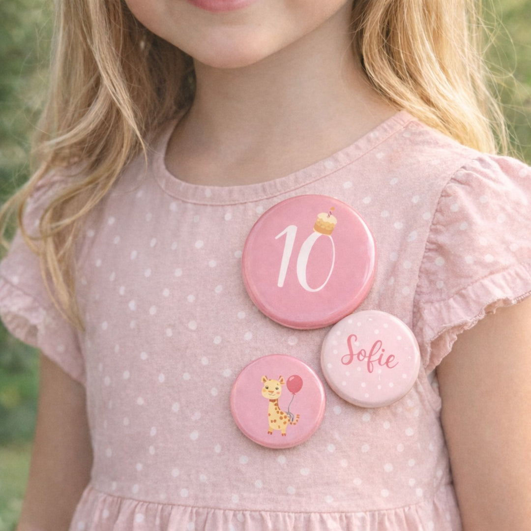 Gepersonaliseerde set van drie verjaardagsbuttons voor een meisje van 10 jaar met het getal 10, de naam Sofie en een girafillustratie, gedragen op een roze jurkje.