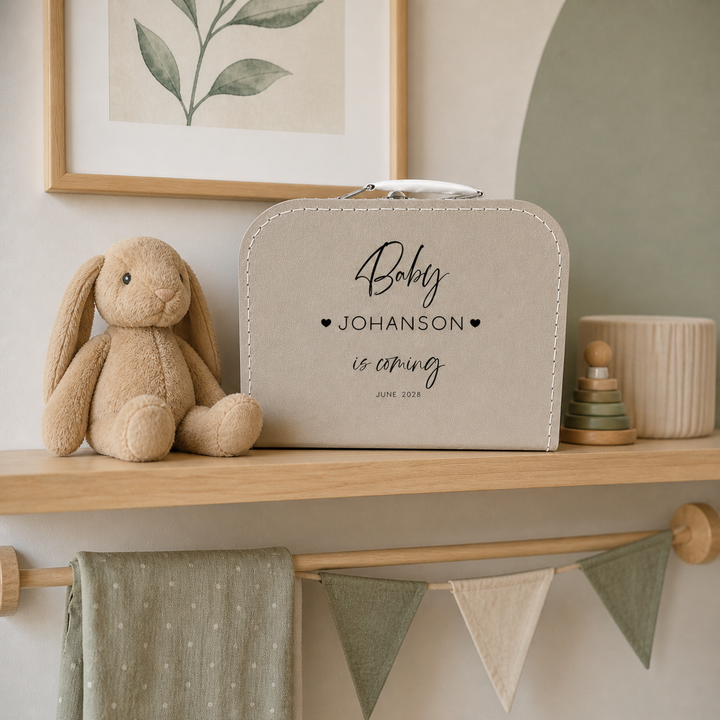 Zwangerschapsaankondiging koffertje “Baby is coming” met naam in kinderkamer naast knuffel, originele zwangerschapsaankondiging