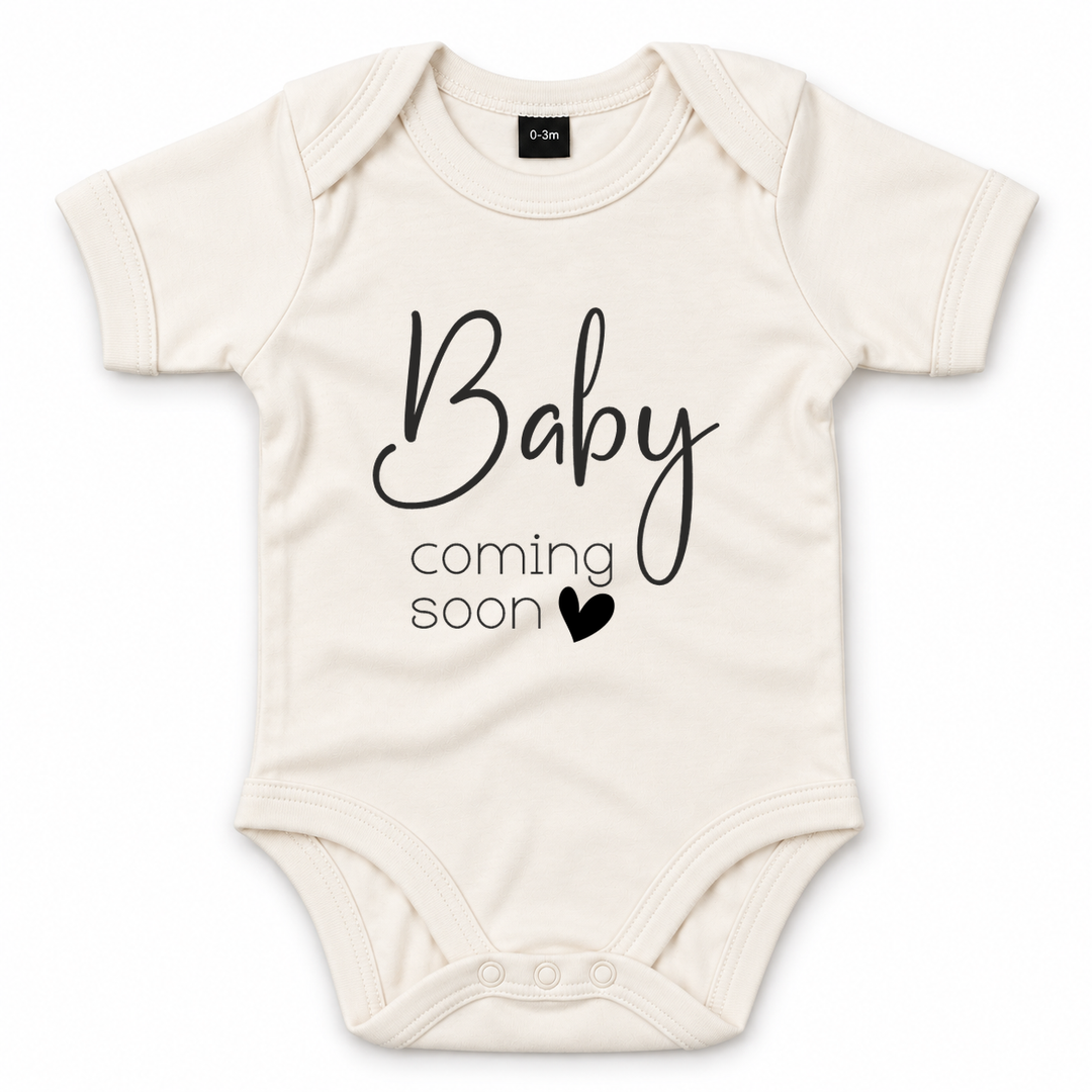 Naturel zwangerschapsaankondiging romper met zwarte tekst Baby Coming Soon en hartje.