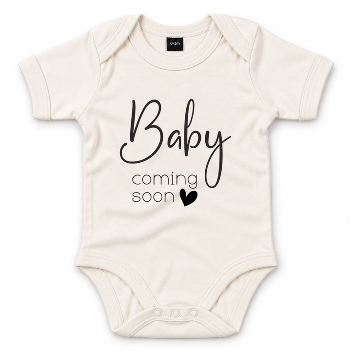 Naturel zwangerschapsaankondiging romper met zwarte tekst Baby Coming Soon en hartje.
