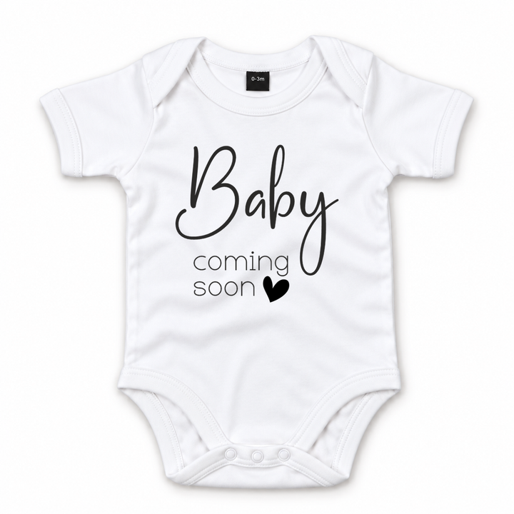 Witte zwangerschapsaankondiging romper met zwarte Baby Coming Soon opdruk.