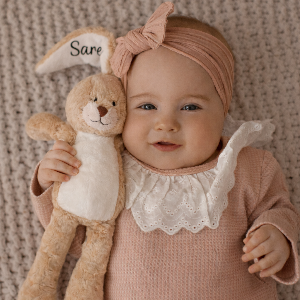 Baby knuffelt een beige gepersonaliseerd konijn met naam Sare op het oor – ideaal als eerste knuffel