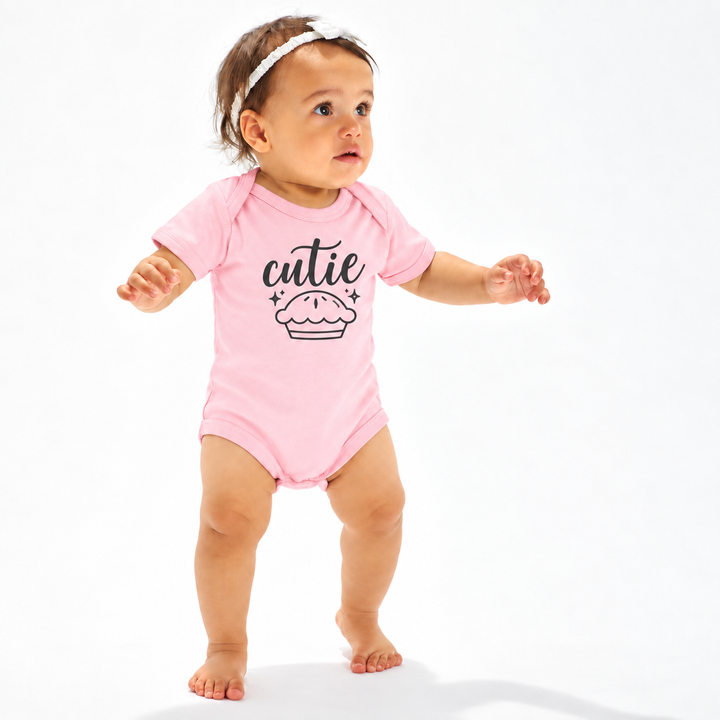 Meisje in roze babyrompertje met tekst Cutie en illustratie van een taartje