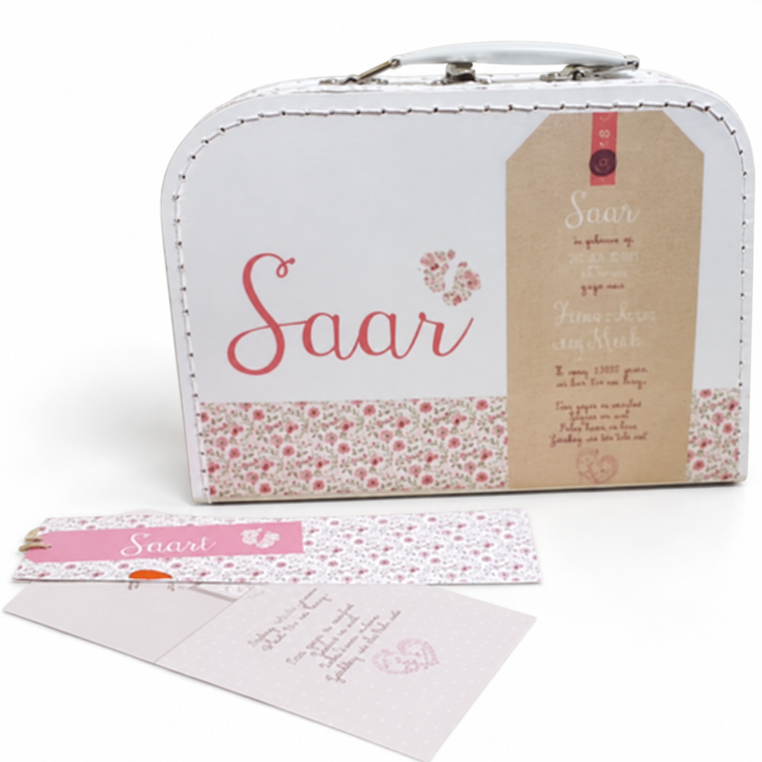 Wit koffertje met de naam Saar, roze bloemetjes en een labelvorm met huisje, met het geboortekaartje ervoor.