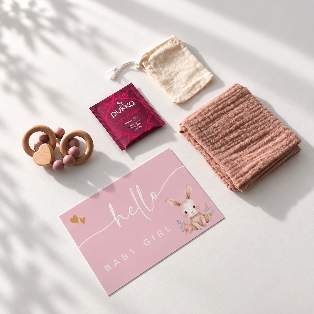 Roze kraamcadeauset voor baby girl van bovenaf met bijtring, hydrofiele doek, thee, cadeaukaart en katoenen zakje.