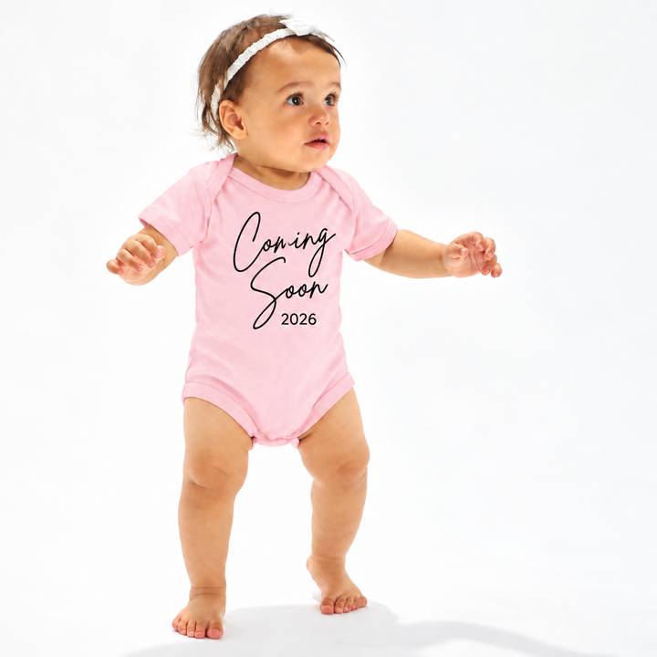 Roze zwangerschapsaankondiging rompertje met Coming Soon 2026 gedragen door baby.