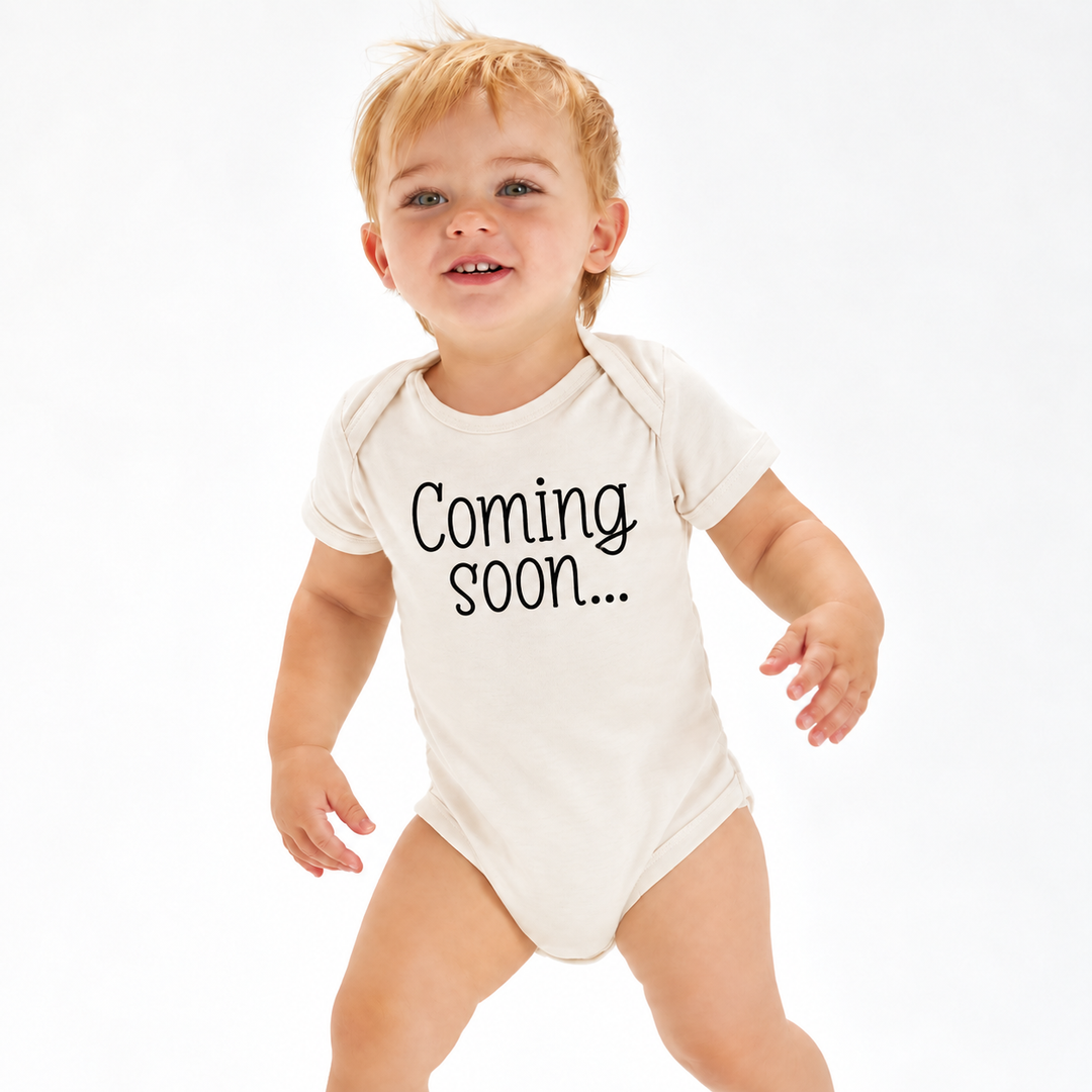 Baby in naturel zwangerschapsaankondiging rompertje met Coming Soon tekst.