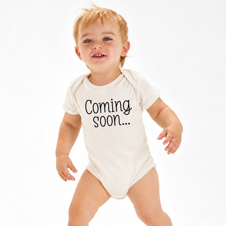 Baby in naturel zwangerschapsaankondiging rompertje met Coming Soon tekst.