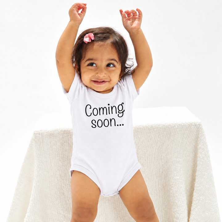 Baby in wit zwangerschapsaankondiging rompertje met Coming Soon tekst.