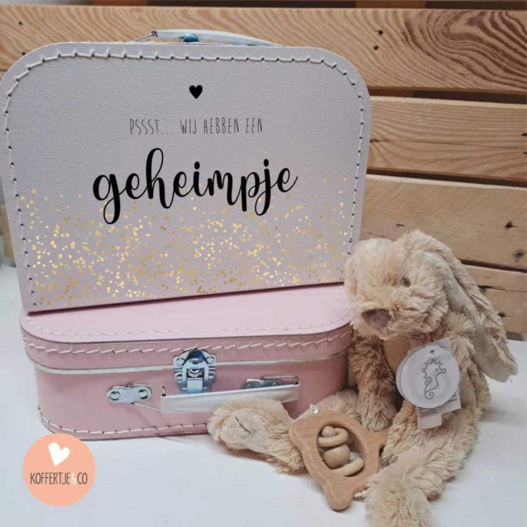 zwangerschapsaankondiging koffertje met tekst “pssst… wij hebben een geheimpje” en gouden confetti, origineel cadeau om zwangerschap aan te kondigen